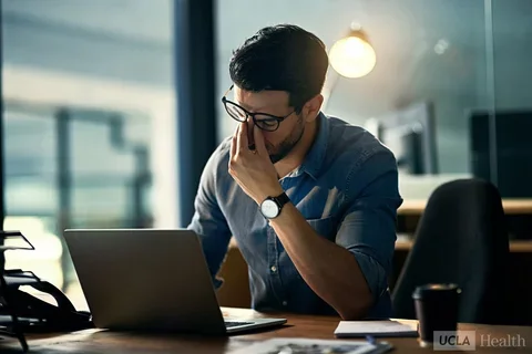 Man looking at his laptop pinching the bridge of his nose in exhausted frustration.