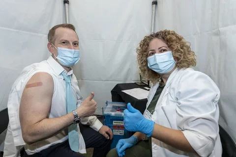 Doctor and patient both giving a "thumbs up" after the patient recieved a vaccination. The man has his arm exposed and a bandage over the injection site.
